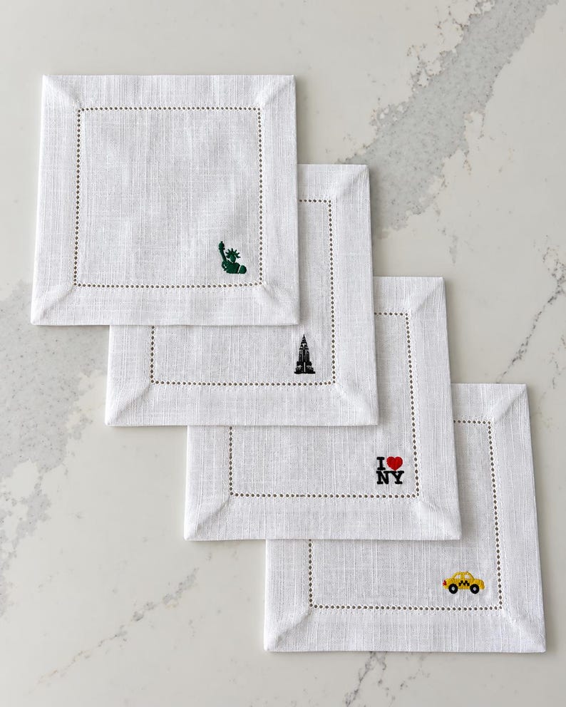 Set of four white hemstitch cocktail napkins embroidered with New York City motifs